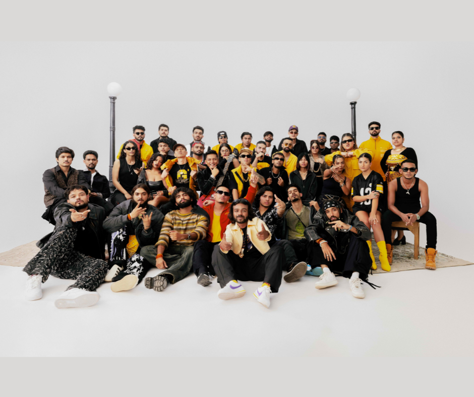 A large group of Indian hip-hop artists, dressed in stylish streetwear, posing together in a studio setting with a white background